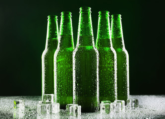 Glass bottles of beer with ice cubes on dark background