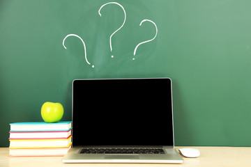 Laptop on table, on green blackboard background