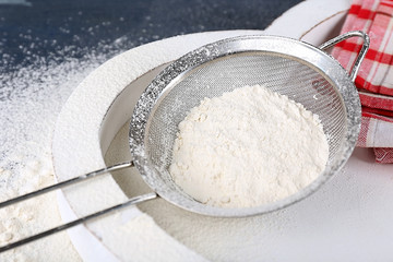 Sifting flour through sieve on wooden table, closeup