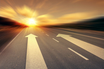 arrow on the road with rising sun on background 
