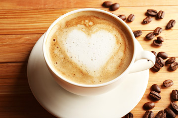 Cup of coffee latte art with grains on wooden table, closeup