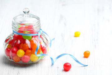 Colorful candies in jar on wooden background