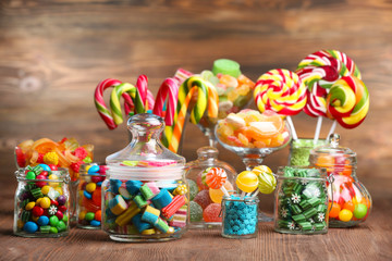 Fototapeta premium Colorful candies in jars on table on wooden background