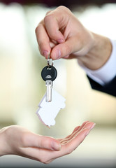 Hand of businessman giving keys to female hand on blurred background