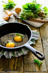 Scrambled eggs with nettles in the pan on wooden table