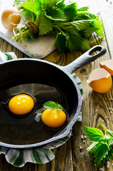 Scrambled eggs with nettles in the pan on wooden table