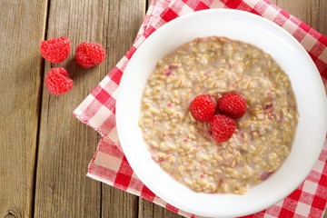 Breakfast oatmeal with raspberries on wood with checkered cloth.
