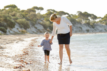 young mother holding sweet blond daughter walking on beach