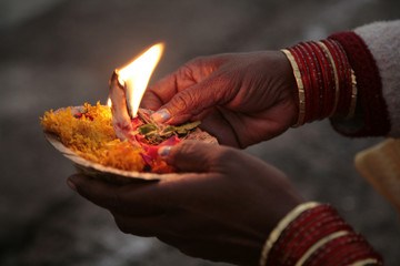 Indian woman hands holding a plate of flowers and burning candle
