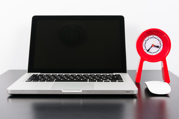 Laptop and red clock  on black wooden table