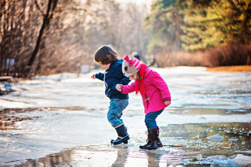 toddler boy and girl walking in early spring puddle