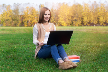 Student sitting on green grass with opened notebook lying on the