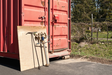 Ein Standrohr für Bauwasser lehnt an einem Materialcontainer