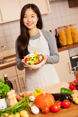 Asian smiling woman with a colorful salad in her hands is standi