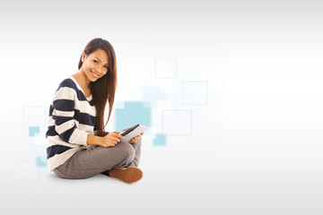 Smiling asian girl with tablet pc is sitting on the floor over w