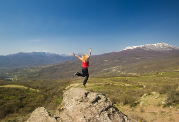 girl jumping with hands up in the mountains against sun