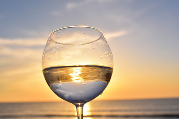 glass with white wine above sunset sea ocean