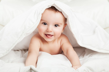 Fototapeta na wymiar Funny and cute little baby smiling under white blanket.