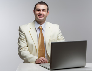 A man in a white suit sitting with a laptop. Makes hand gestures