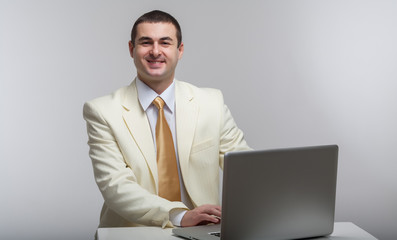 A man in a white suit sitting with a laptop. Makes hand gestures