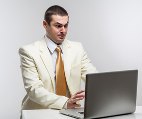 A man in a white suit sitting with a laptop. Makes hand gestures