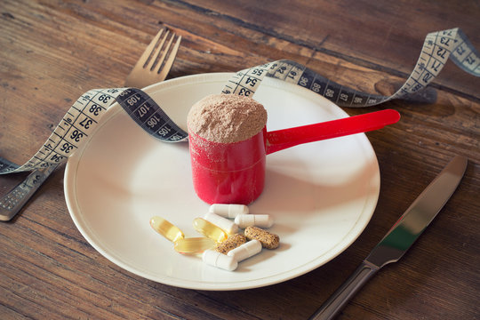 Whey protein powder in scoop with vitamins on plate