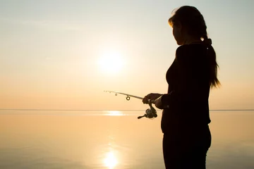 Foto op Plexiglas Vissen silhouette of a young girl fishing at sunset near the sea