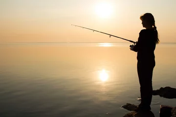 Foto op Plexiglas silhouet van een jong meisje dat bij zonsondergang in de buurt van de zee vist © fantom_rd