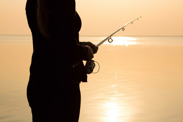 Fisherman silhouette at sunset near the sea with a fishing rod