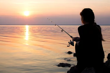 Abwaschbare Fototapete Angeln young girl fishing at sunset near the sea