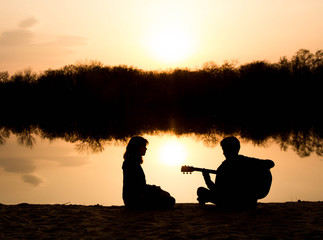 silhouette of a young boy and girl on the beach with a guitar