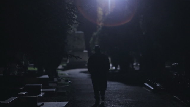 Mysterious man in black cloak and hat going at night in the park
