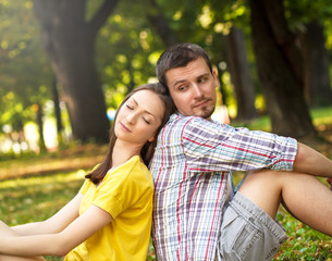 Young couple sitting in park, leaning on each other.