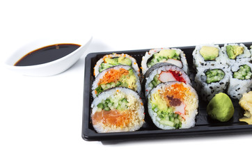 Assorted sushi rolls in a black plastic tray against white backg