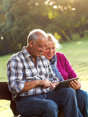 Senior couple sitting on a park bench looking at tablet