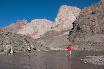 Man with backpack resting on trekking pole moves a river