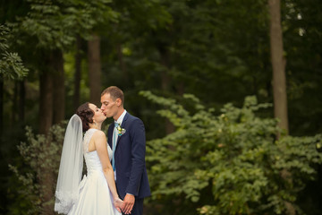 groom and bride in white dress on background of green trees