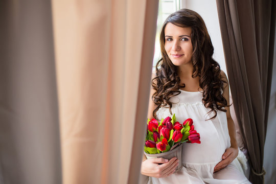 young pregnant woman sit on window with flowers