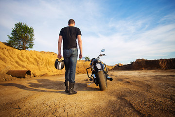 Biker standing with its motorbike on yellow sandy stone at sunse