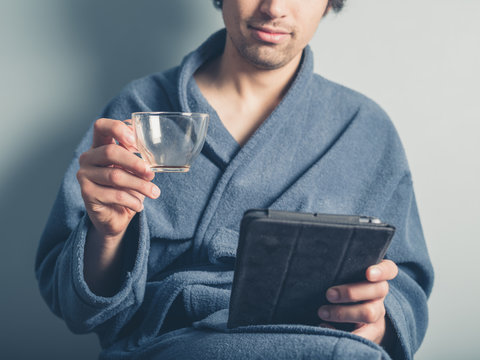 Man in bathrobe with empty cup using tablet