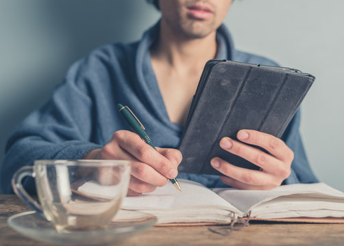 Man in bathrobe using tablet and taking notes