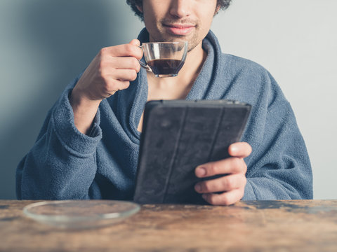 Man in bathrobe having coffee and using tablet