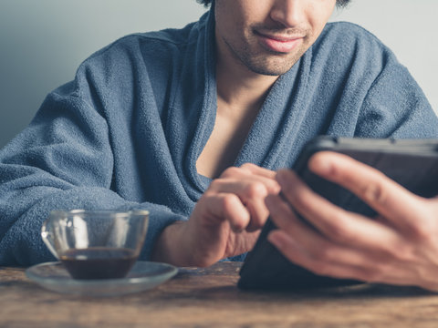 Man in bathrobe having coffee and using tablet