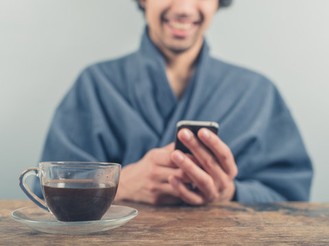 Man in bathrobe using smart phone and drinking coffee