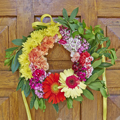 colorful flowers wreath hanging on wooden door closeup