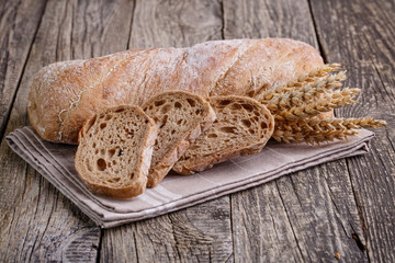 Tasty bread with wheat on wooden background.