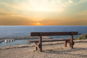 Fototapeta na wymiar Wooden bench on the beach against the setting sun