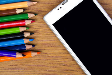 Naklejka premium pencils color and smart phone on wood background, top view
