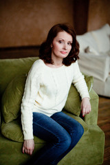 Obraz premium Portrait of mid-adult woman looking at camera sitting in armchair in bright living room