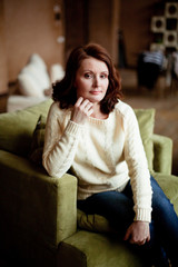 Obraz premium Portrait of mid-adult woman looking at camera sitting in armchair in bright living room